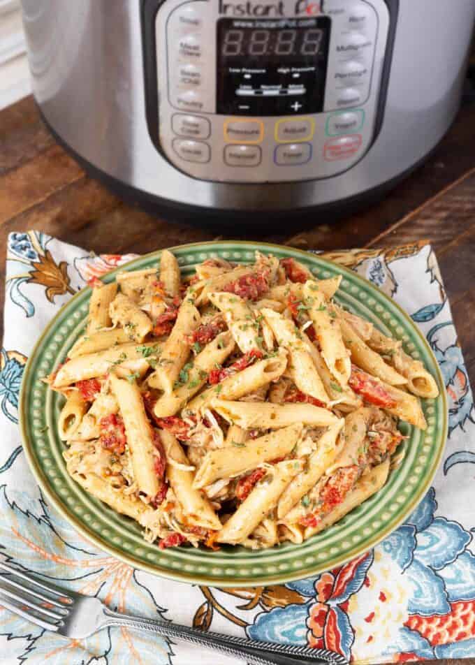 Pressure cooker Pesto Pasta on green plate in front of pressure cooker