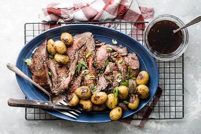 blue plate with sliced beef and small potatoes on a cooling rack