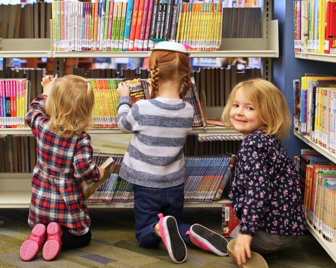 three young girls looking for books at a library