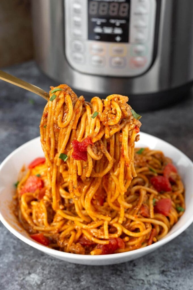Instant Pot Taco Spaghetti in a white bowl with a forkful, in front of the pot