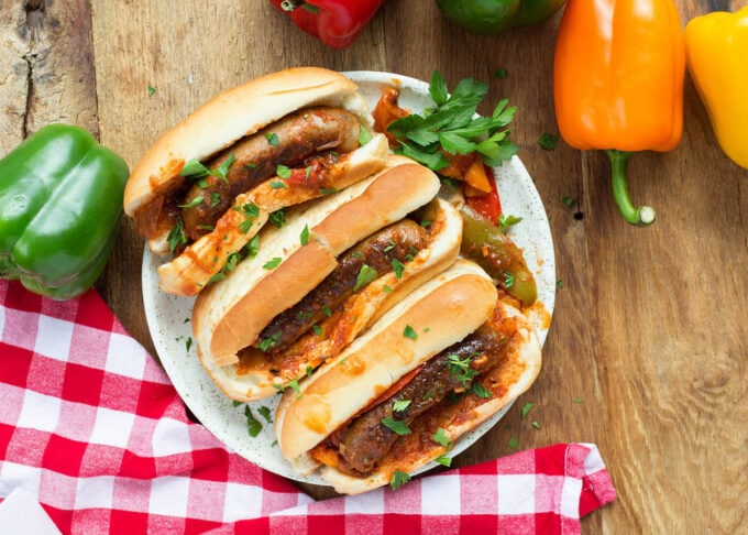 three sausage and peppers on hoagie rolls on a white plate on a wood background