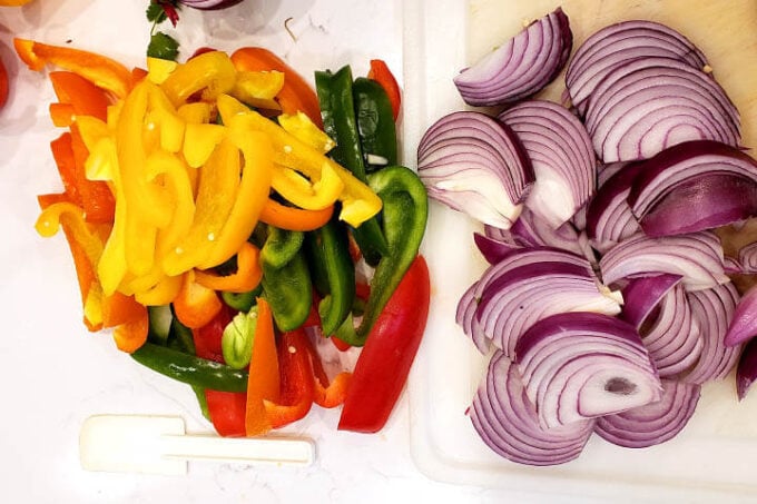 sliced bell peppers and red onion on a white cutting board from above