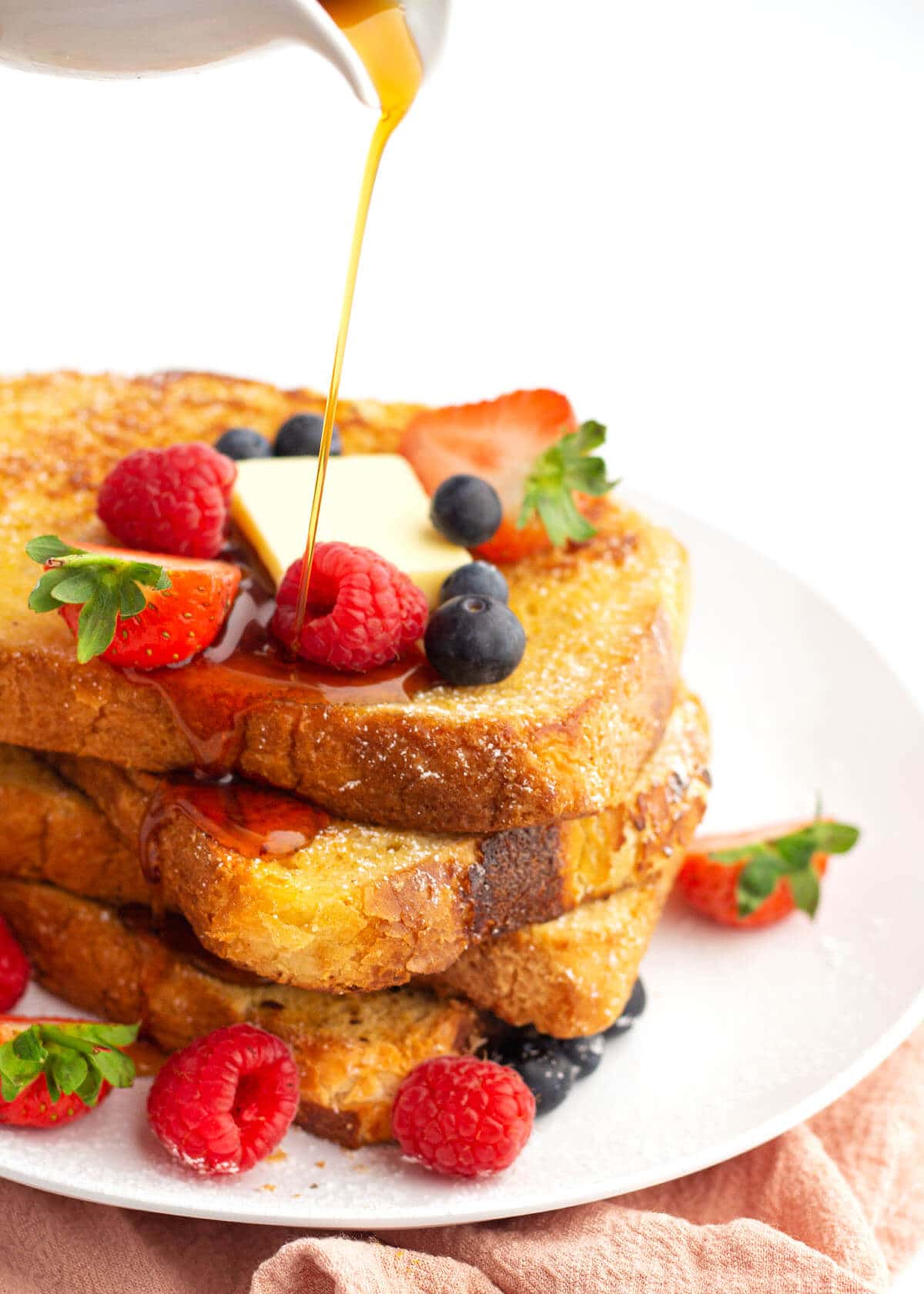 stack of french toast with berries and syrup pouring on them