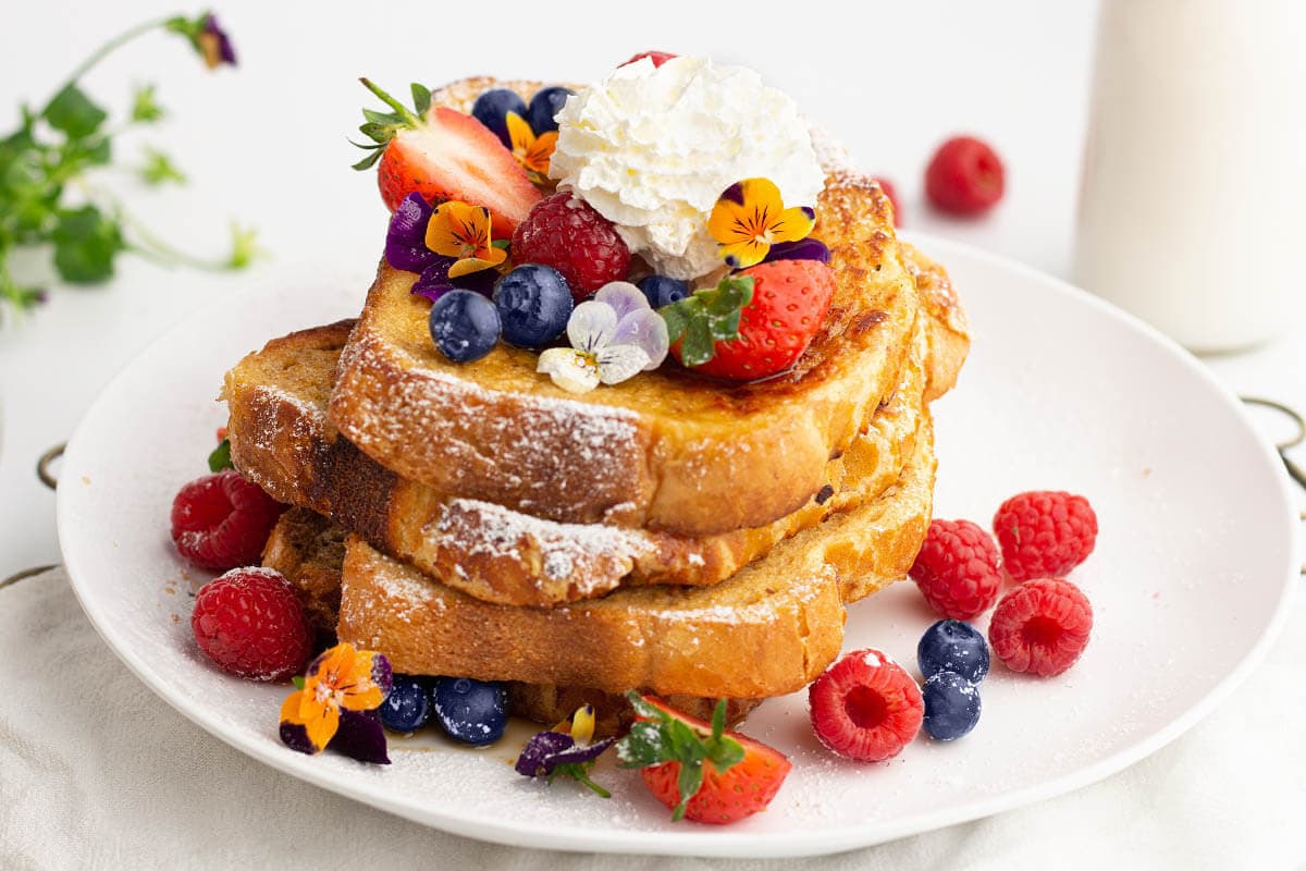 stack of air fryer french toast with berries, butter, syrup on them