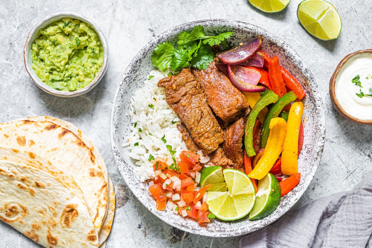 Air Fryer Fajitas with tortillas and garnishes on a grey plate