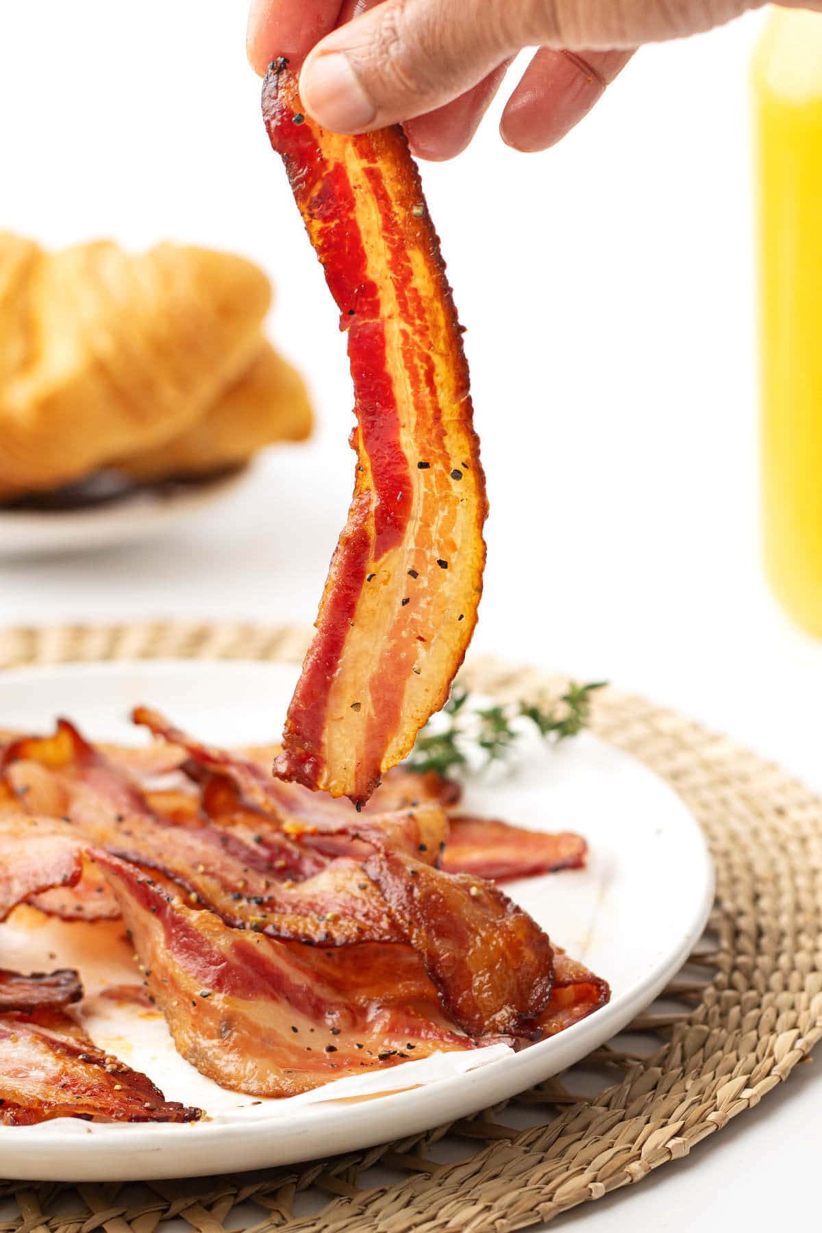 hand holding a slice of air fryer bacon above plate of bacon