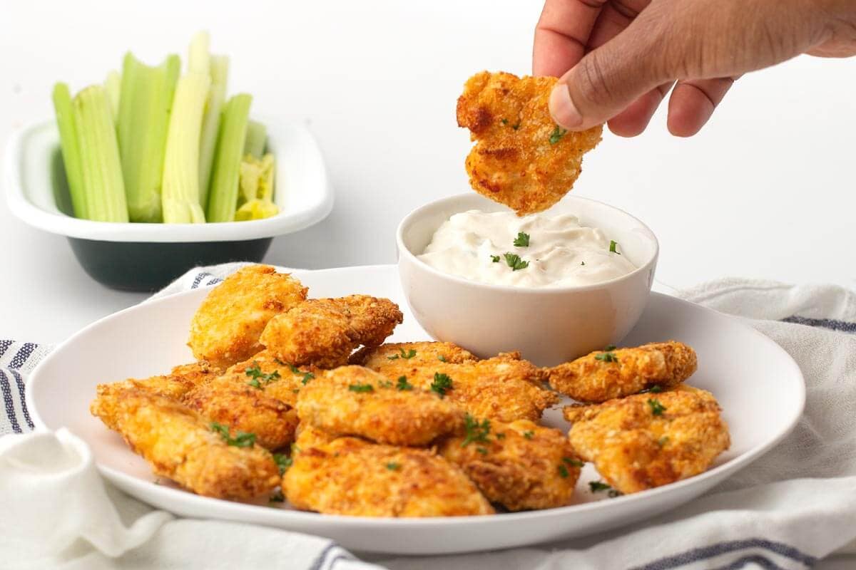 dipping nugget into dip with plate of nuggets