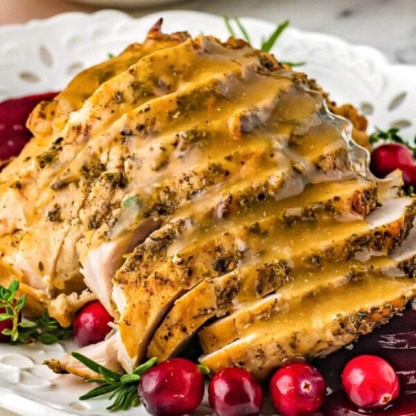 sliced turkey breast with gravy on a white plate with cranberries