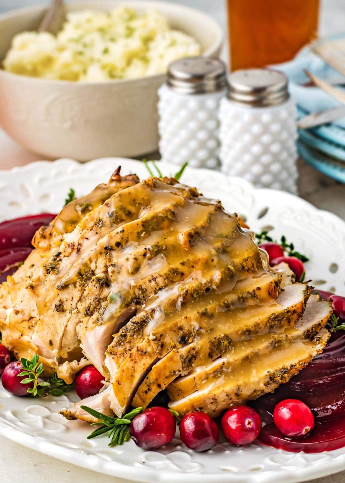 sliced turkey breast on a white plate with gravy and cranberries