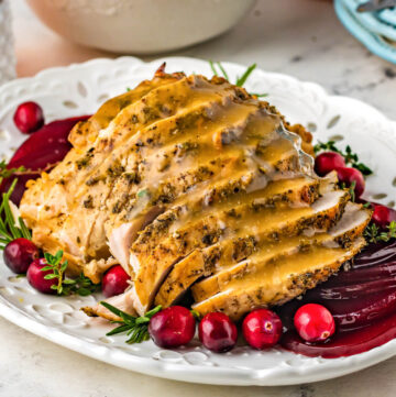 sliced turkey breast with gravy on a white plate with cranberries