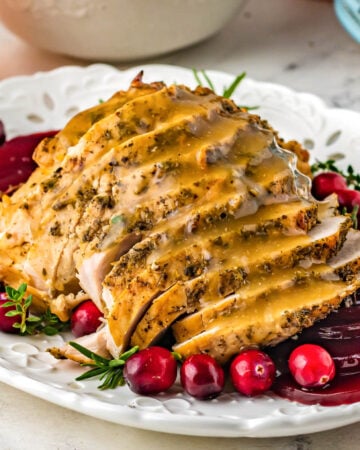 sliced turkey breast with gravy on a white plate with cranberries