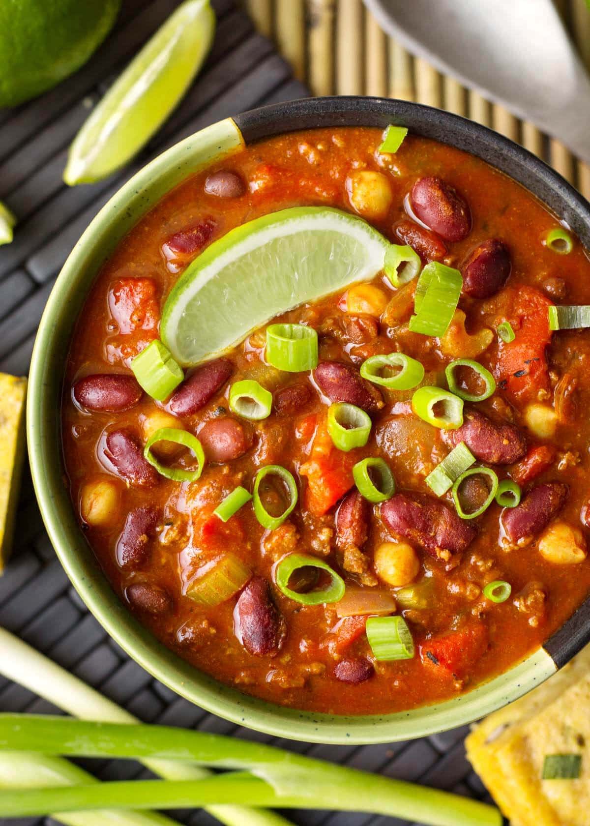 a bowl of chili with lime wedge and green onion.