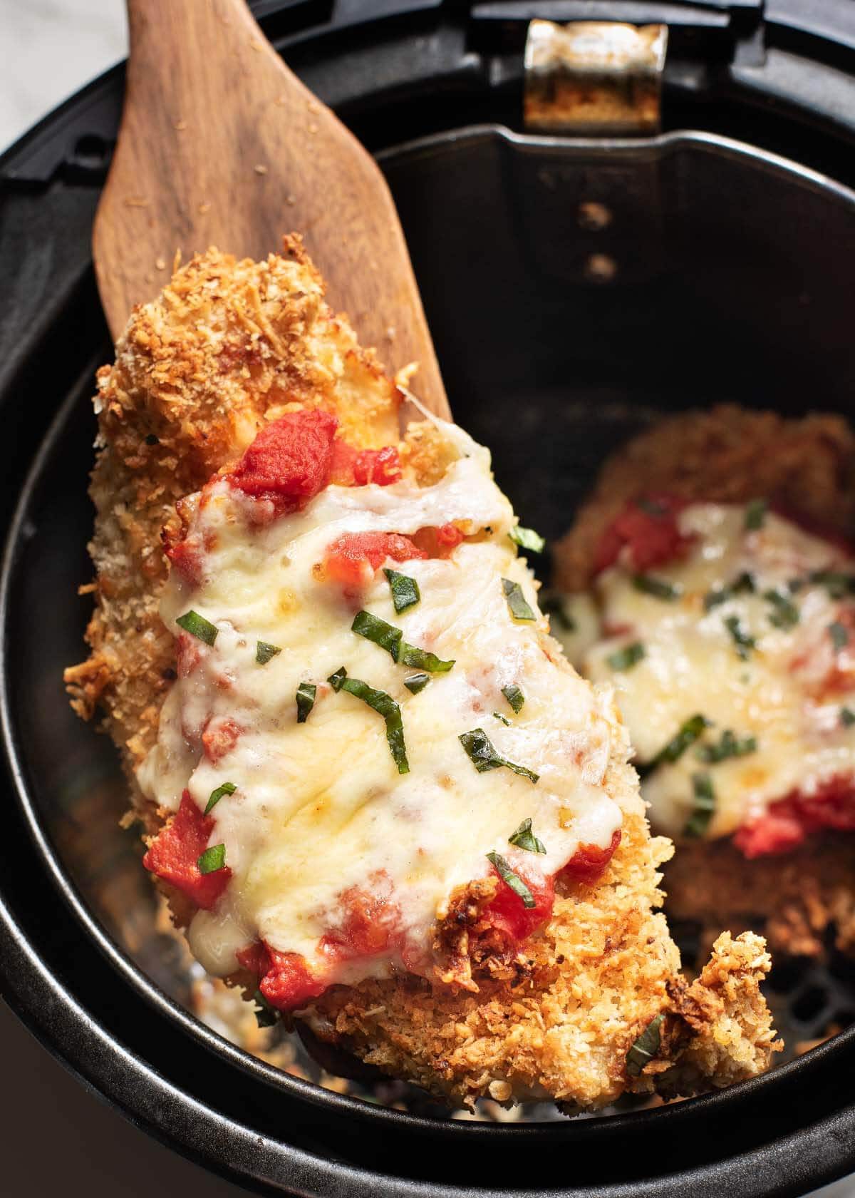 Chicken Parmesan in air fryer basket, on a wood spatula