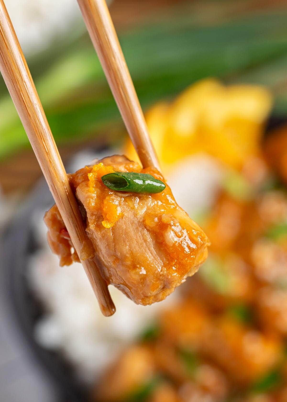 Instant Pot Orange Chicken bite held in chopsticks.