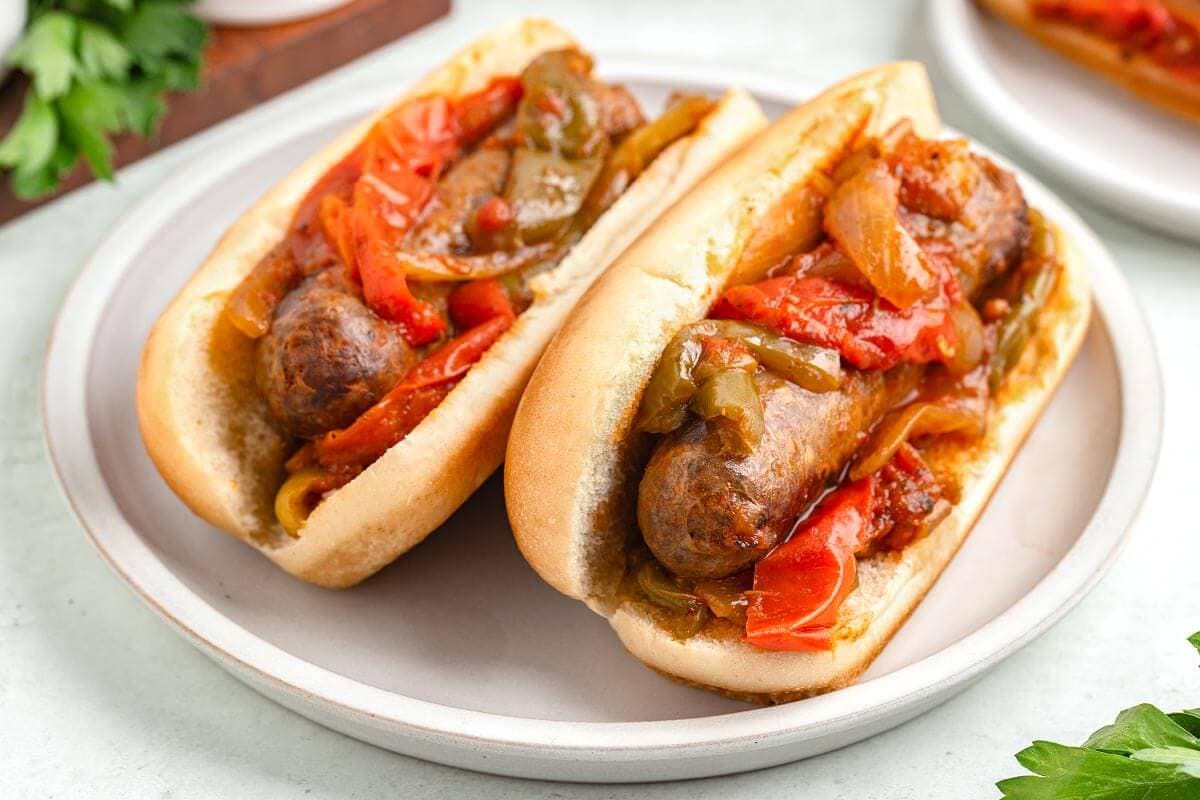 two Sausage and Peppers in  buns on a white plate