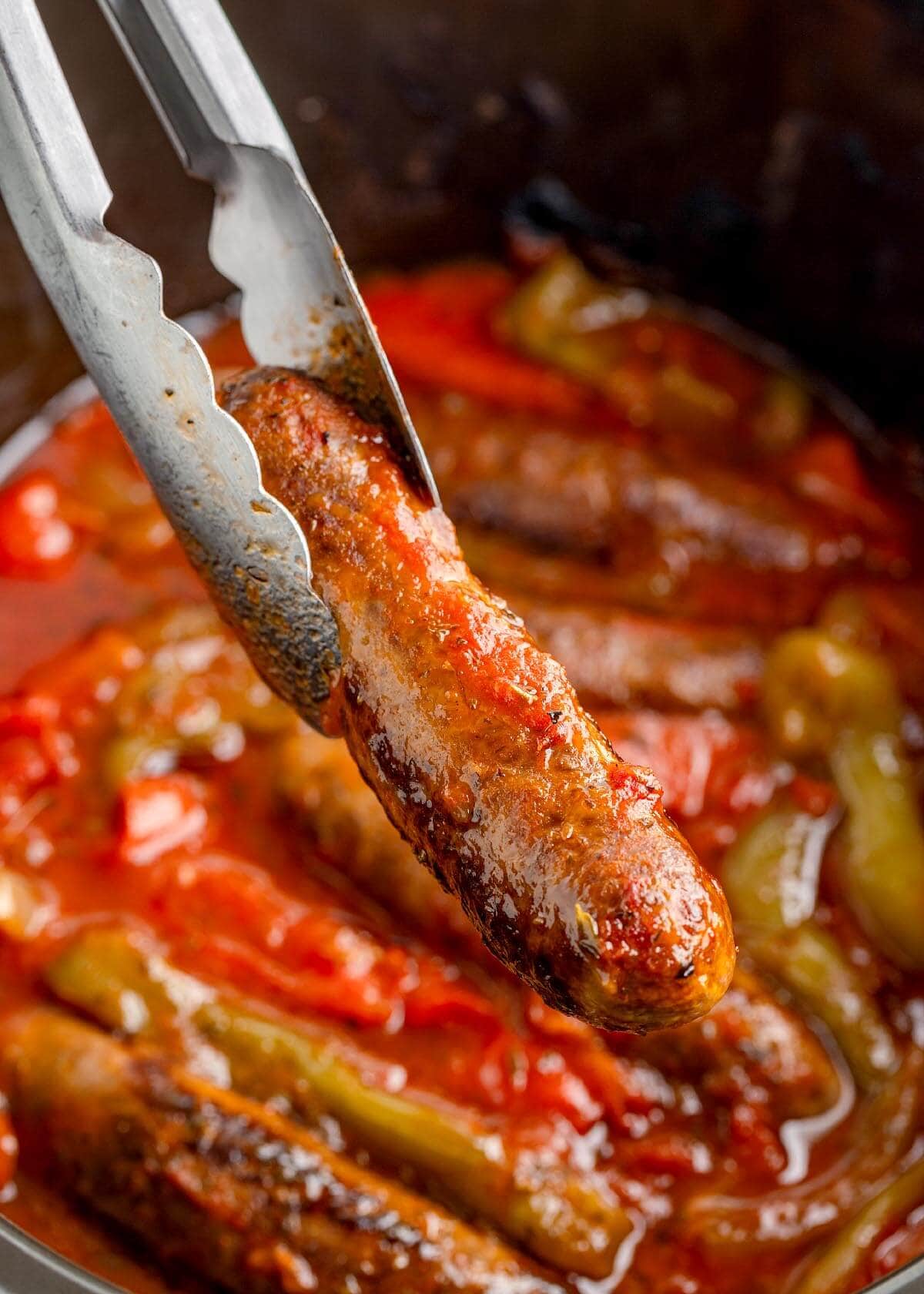 tongs holding a sausage in crock