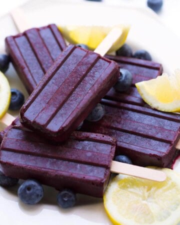 Five Blueberry Lemon Popsicles on a white plate with lemon slices and blueberries