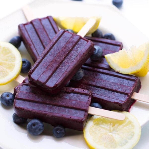 Five Blueberry Lemon Popsicles on a white plate with lemon slices and blueberries