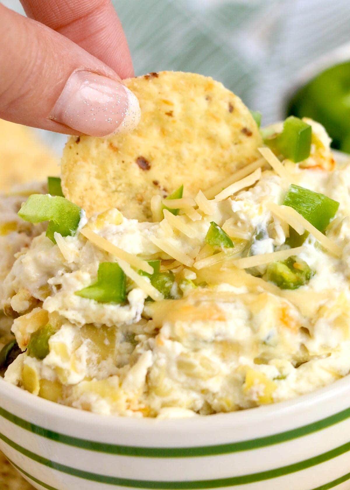dipping chip into bowl of artichoke dip.