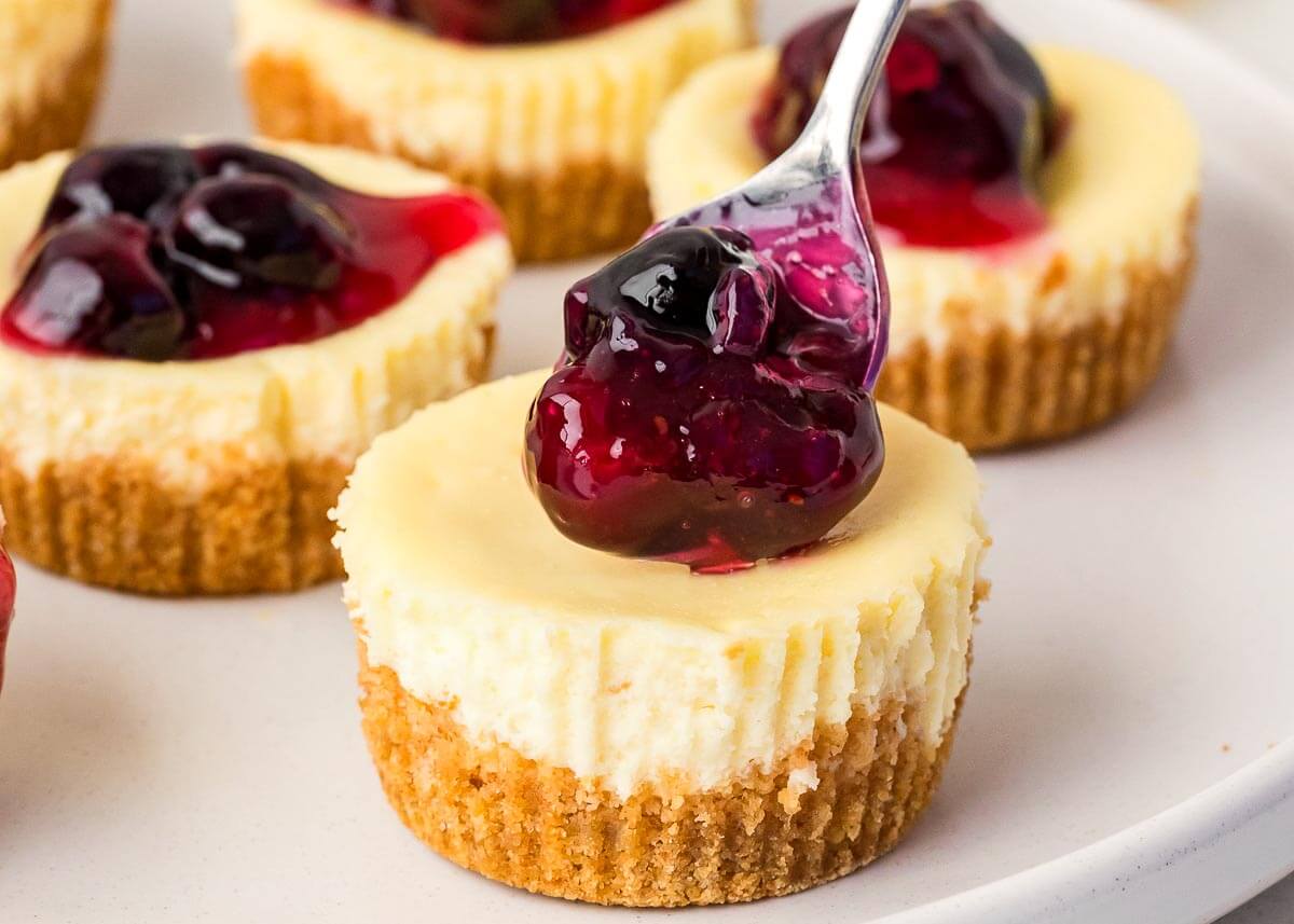 Mini Cheesecakes with blueberry filling on a spoon on white plate.