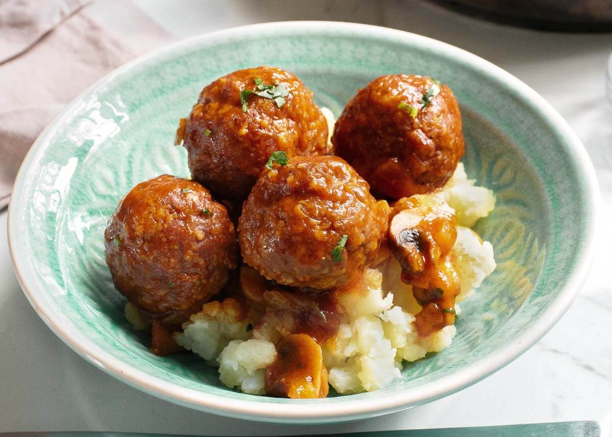 Meatballs in a green bowl on potatoes.