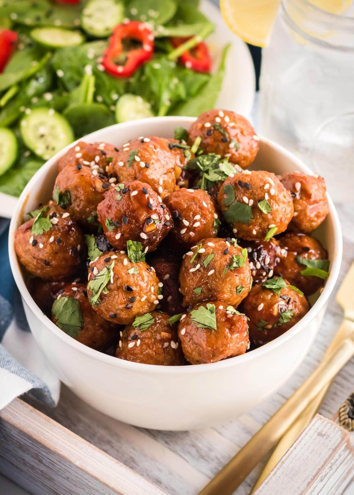 Slow Cooker Honey Garlic meatballs in a white bowl with sesame seeds
