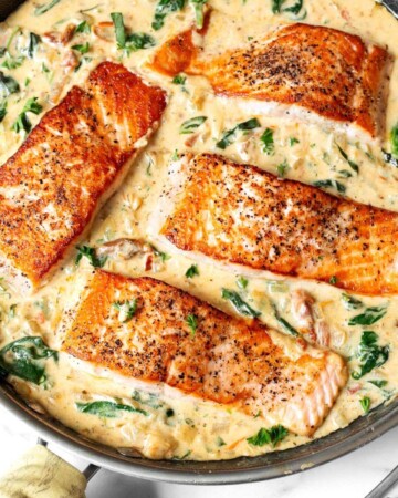 4 Creamy Garlic Tuscan Salmon filets in a pan of sauce.