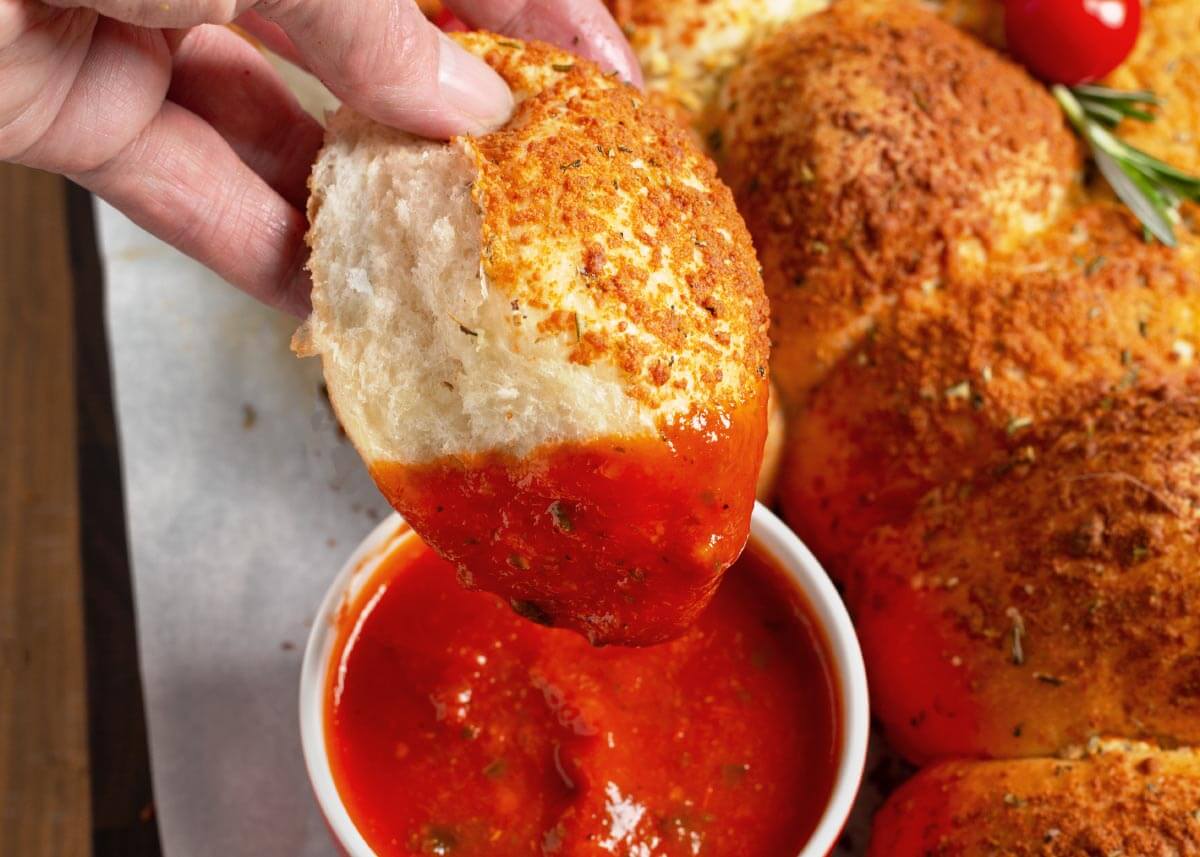 dipping Dinner Roll Christmas Tree Appetizer in marinara sauce.