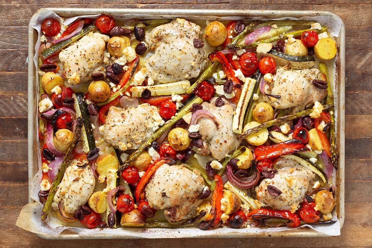 Sheet pan with Greek chicken thighs, potatoes, cherry tomatoes, olives, and feta