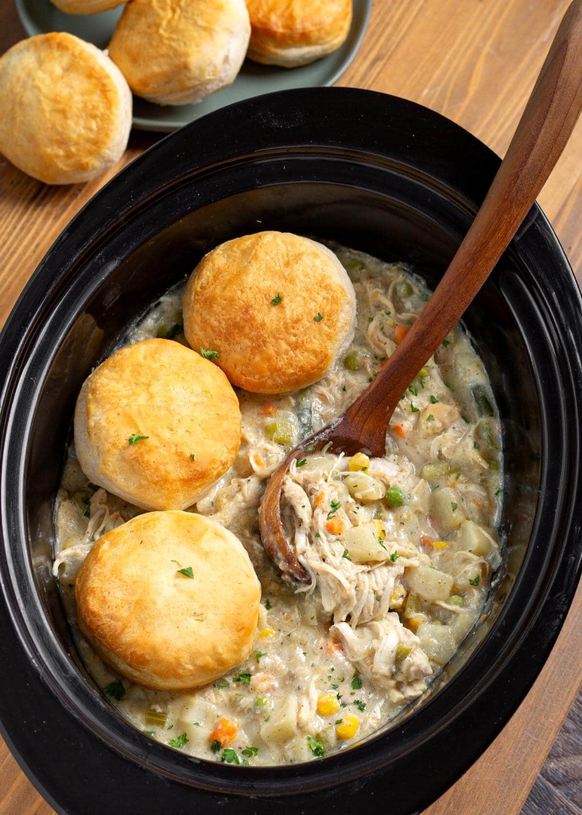 Slow Cooker Chicken Pot Pie with 3 biscuits in a black crock.
