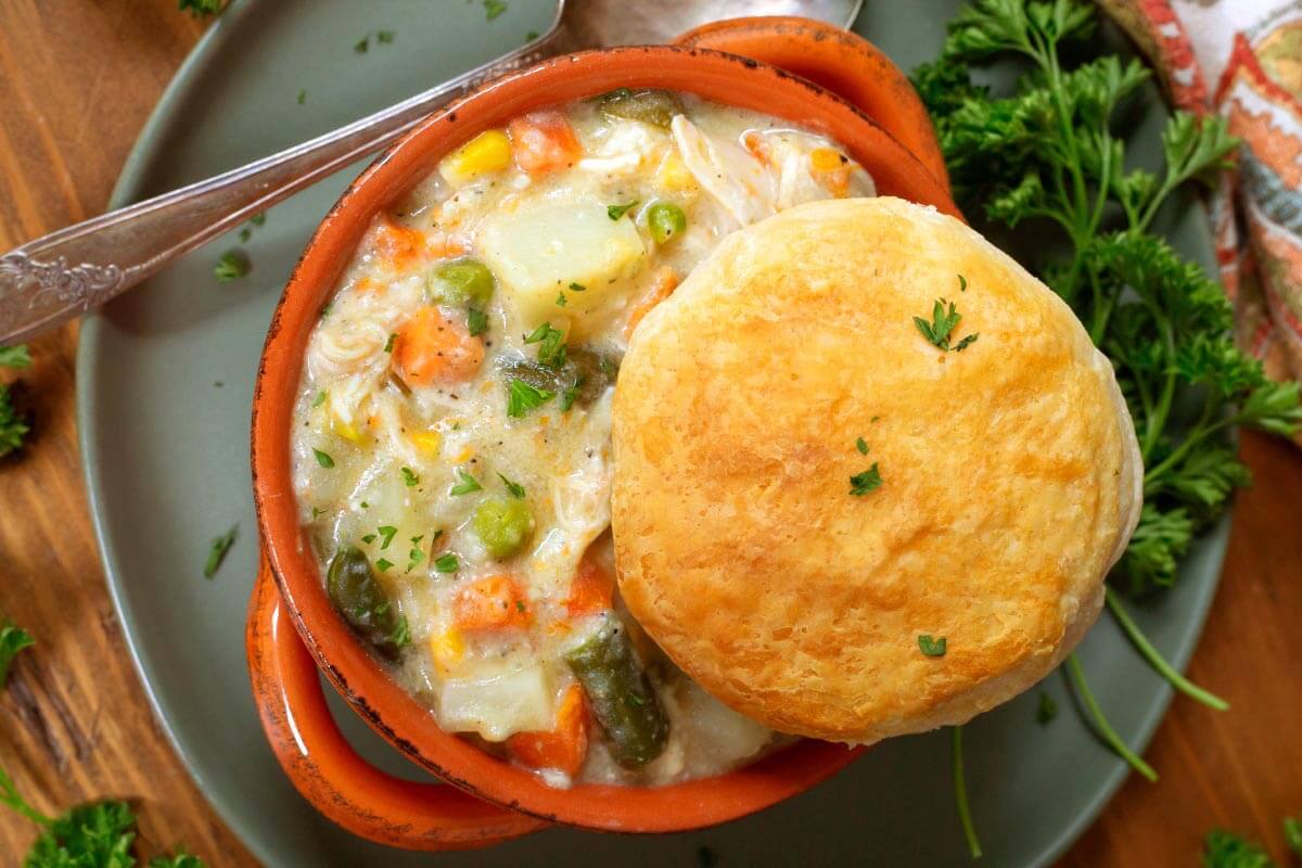 Slow Cooker Chicken Pot Pie in an orange bowl with biscuit on top.