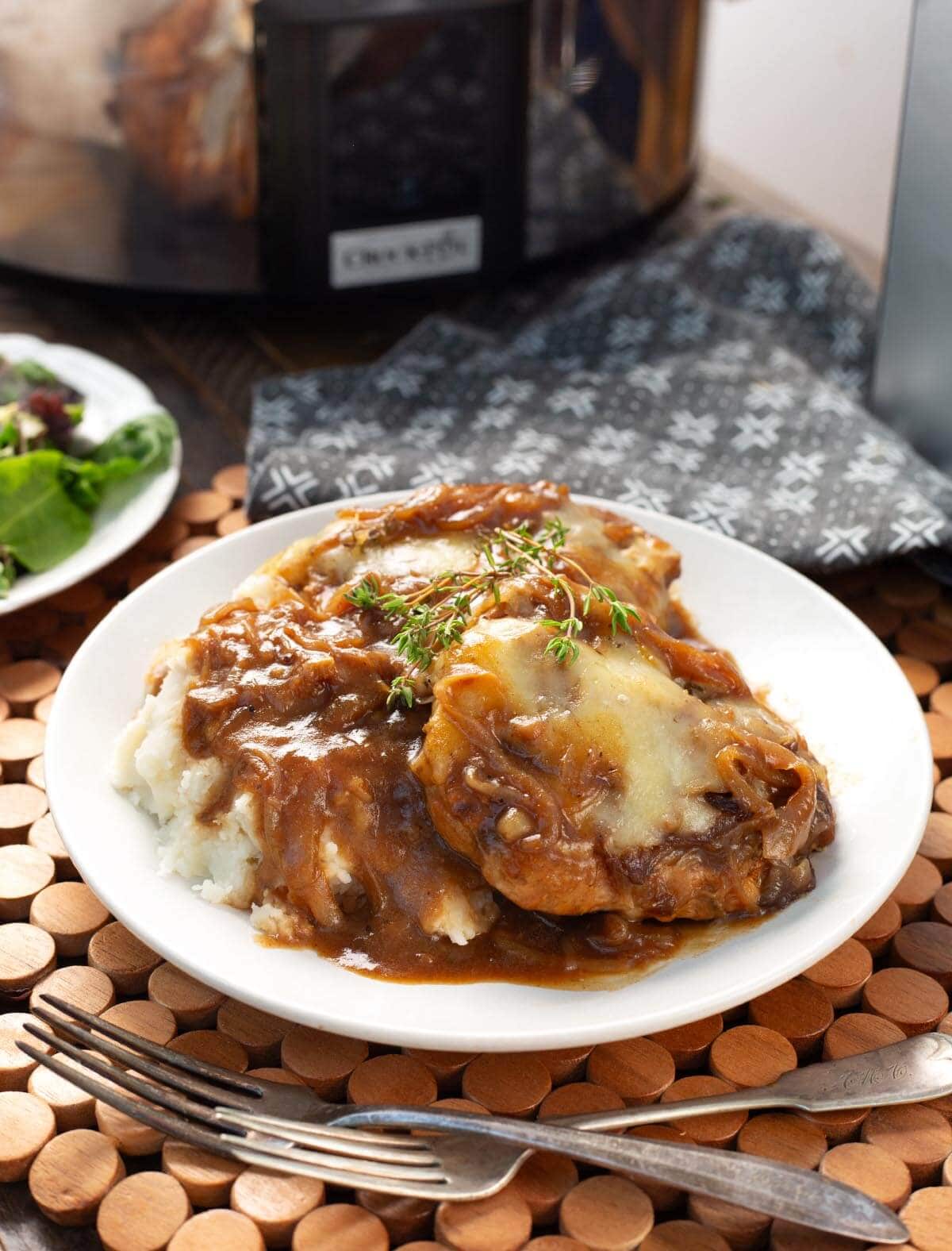 Slow Cooker French Onion Pork Chops on a white plate with potatoes and gravy.