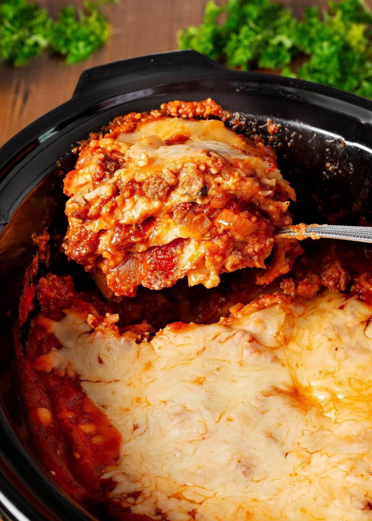 Slow Cooker Lasagna on a spoon in black crock.