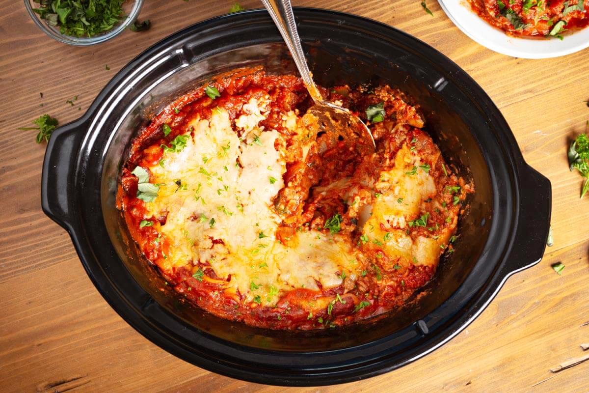 Slow Cooker Lasagna with a spoon in black crock.