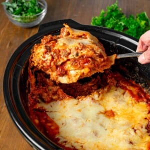 Slow Cooker Lasagna in a black crock with serving on a spatula.