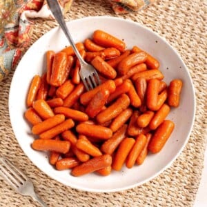 Slow Cooker Maple Brown Sugar Carrots in a white bowl with fork.