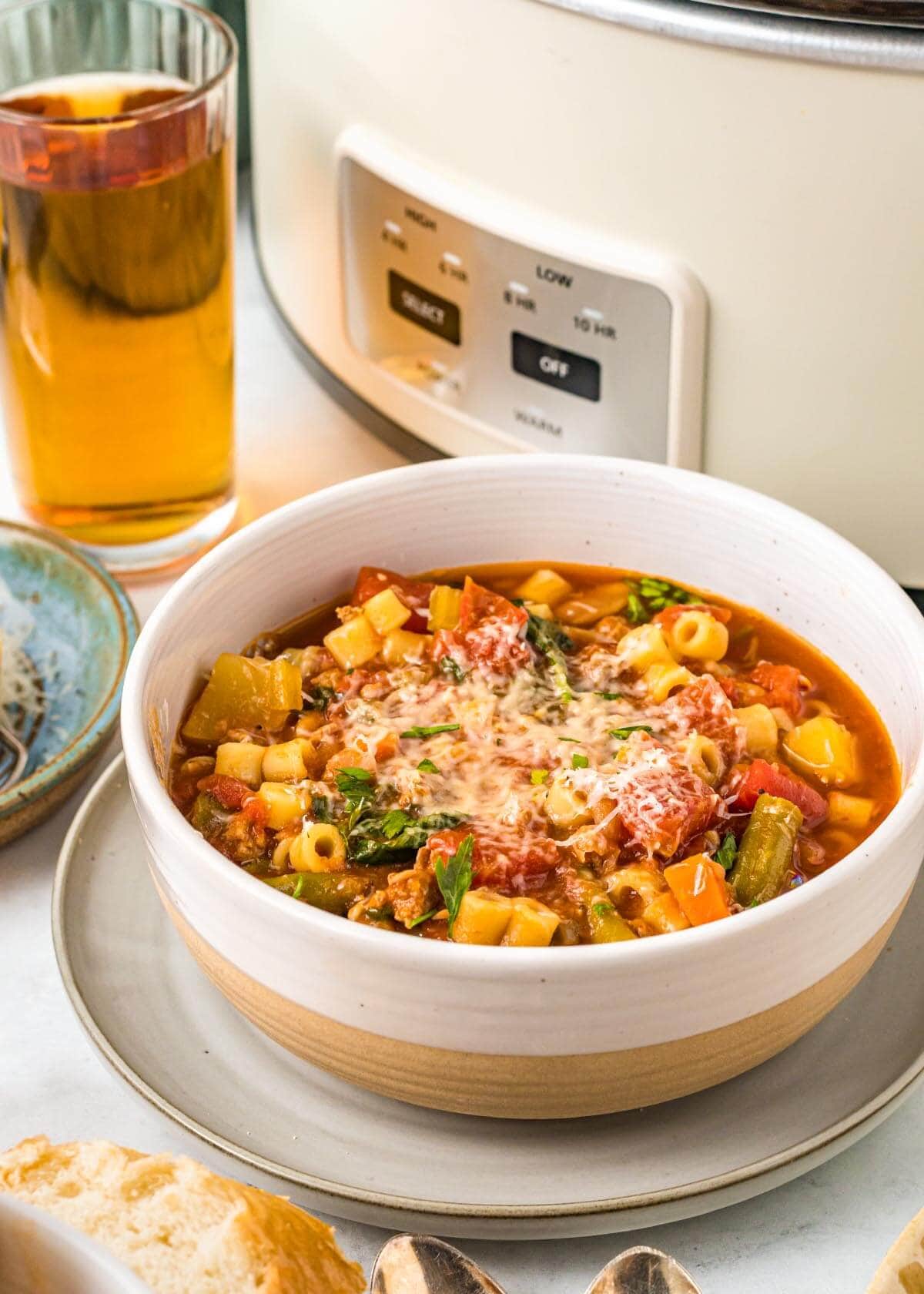 Slow Cooker Minestrone Soup in white bowl in front of crockpot.