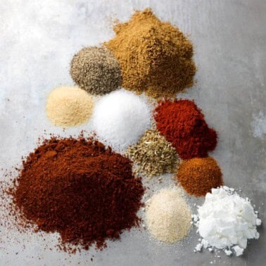 several spices in piles on a grey surface