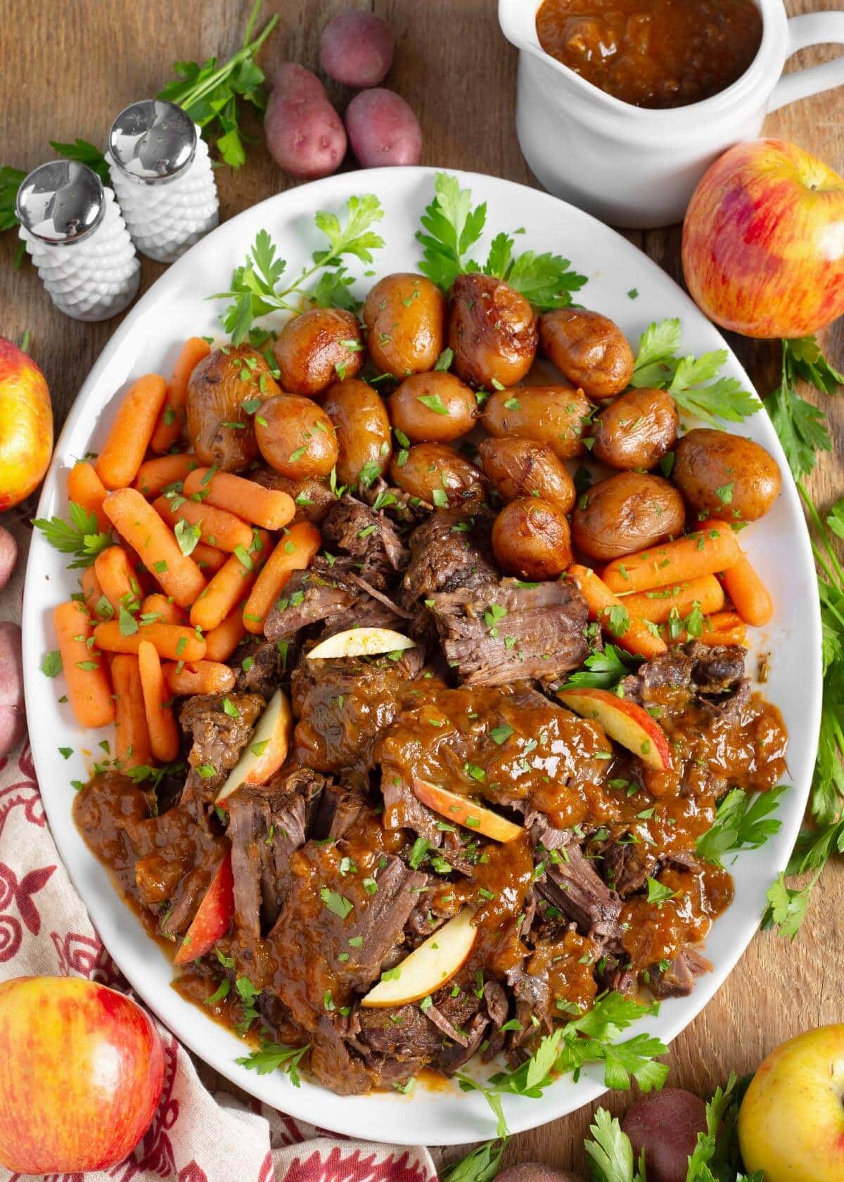 Apple Cider Pot Roast on a white platter with carrots and potatoes.