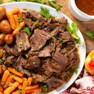 Apple Cider Pot Roast on a white platter with carrots and potatoes.