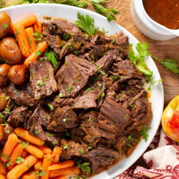 Apple Cider Pot Roast on a white platter with carrots and potatoes.