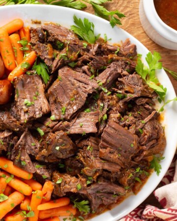 Apple Cider Pot Roast on a white platter with carrots and potatoes.