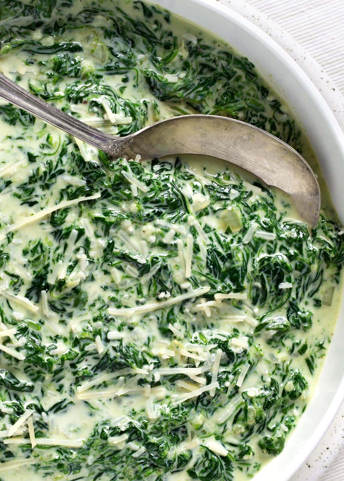 Cheesy Creamed Spinach in a bowl with spoon closeup.