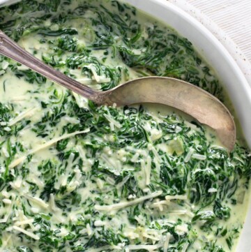 Cheesy Creamed Spinach in a bowl with spoon closeup.