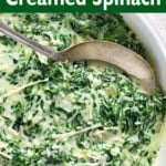 Cheesy Creamed Spinach in a white bowl with spoon closeup