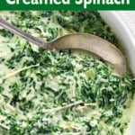 Cheesy Creamed Spinach in a white bowl with spoon closeup