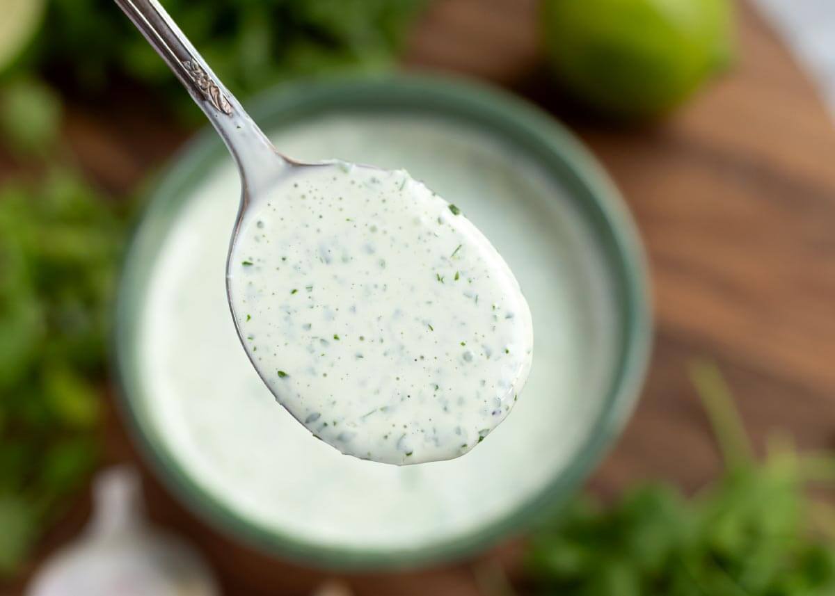 Cilantro Cream Sauce in a green bowl with a spoonful above