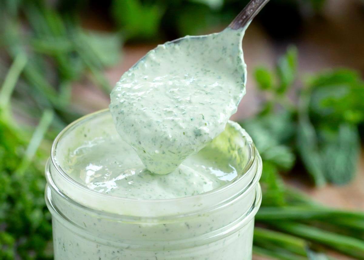 herb yogurt salad dressing in a jar with spoonful above it.