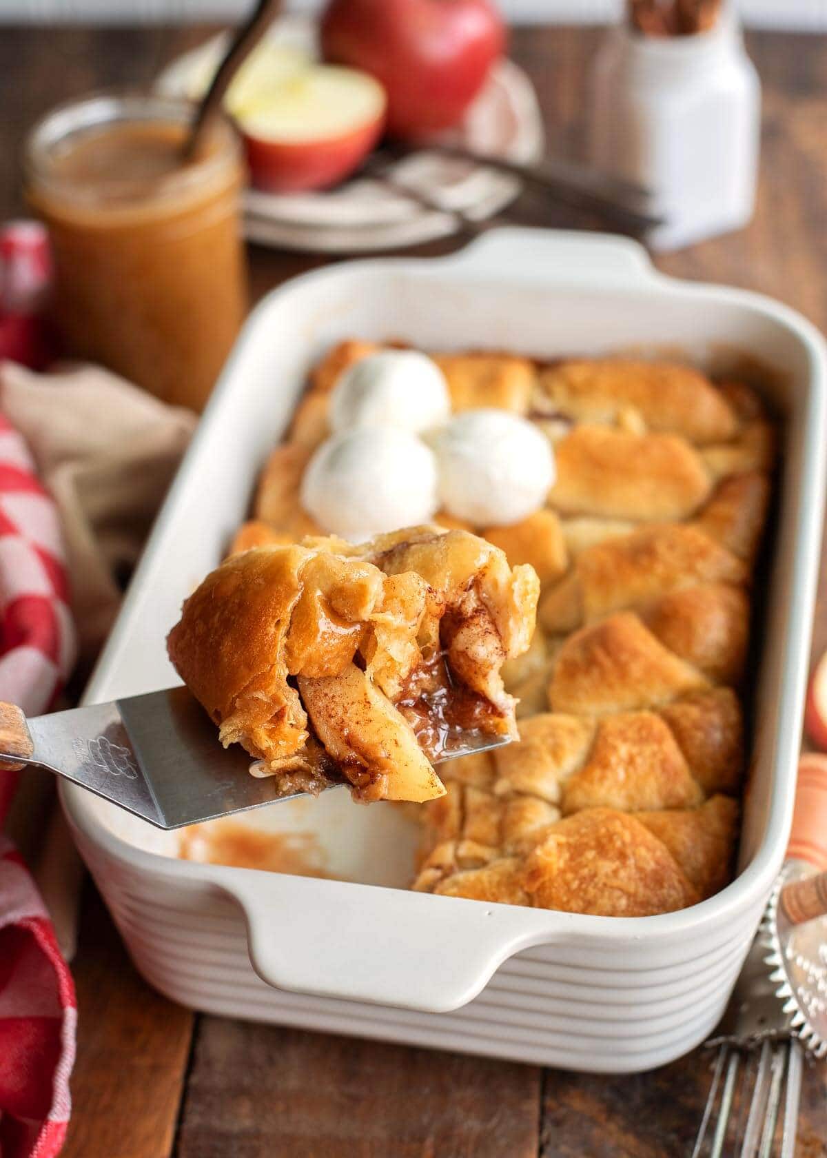 Crescent Roll Apple Dumpling on a spatula in front of pan of them.