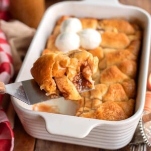 Crescent Roll Apple Dumpling on a spatula in front of pan of them.